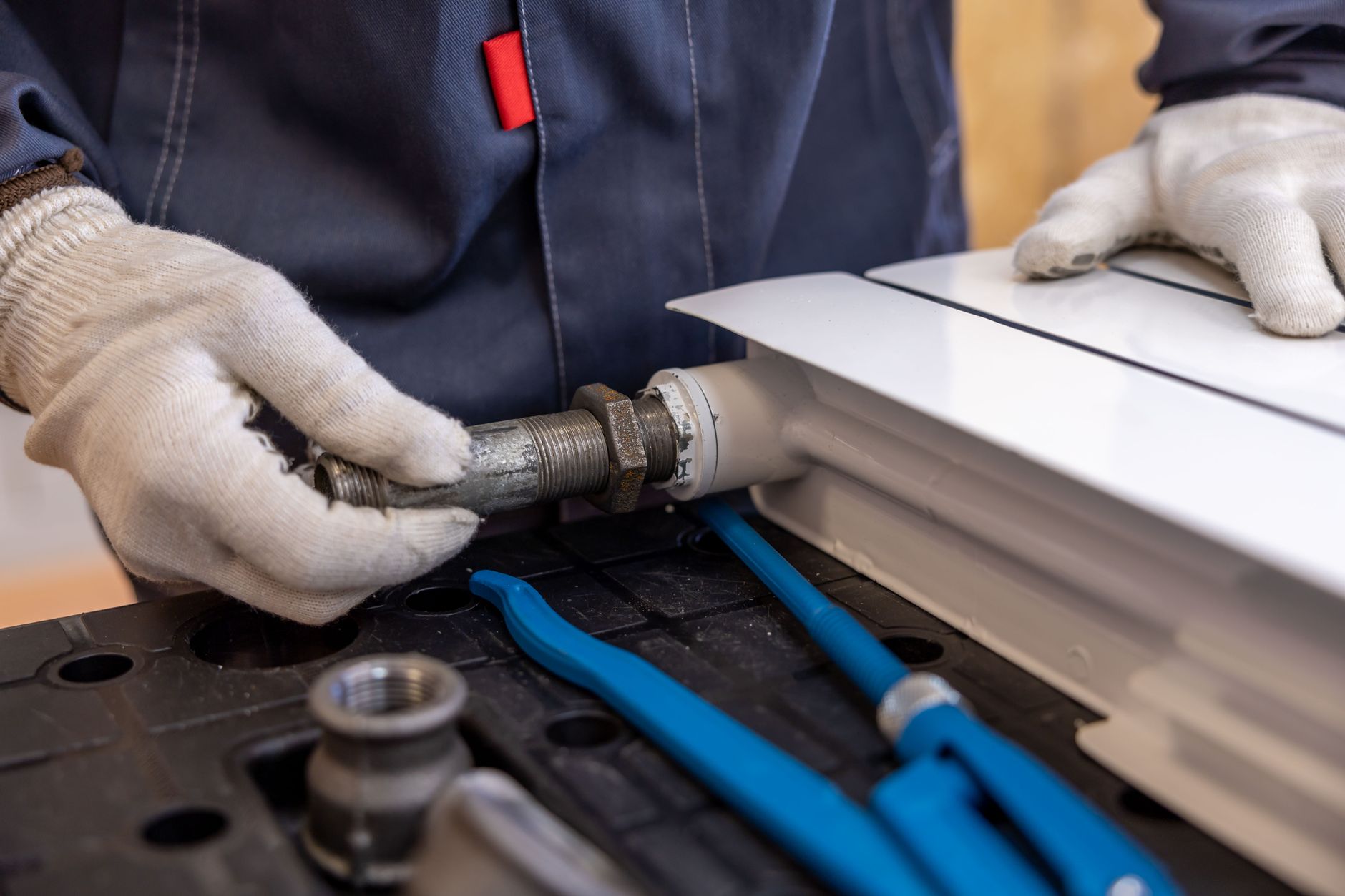 Close-up of gloved hands fitting a metal pipe joint with blue hand tools nearby