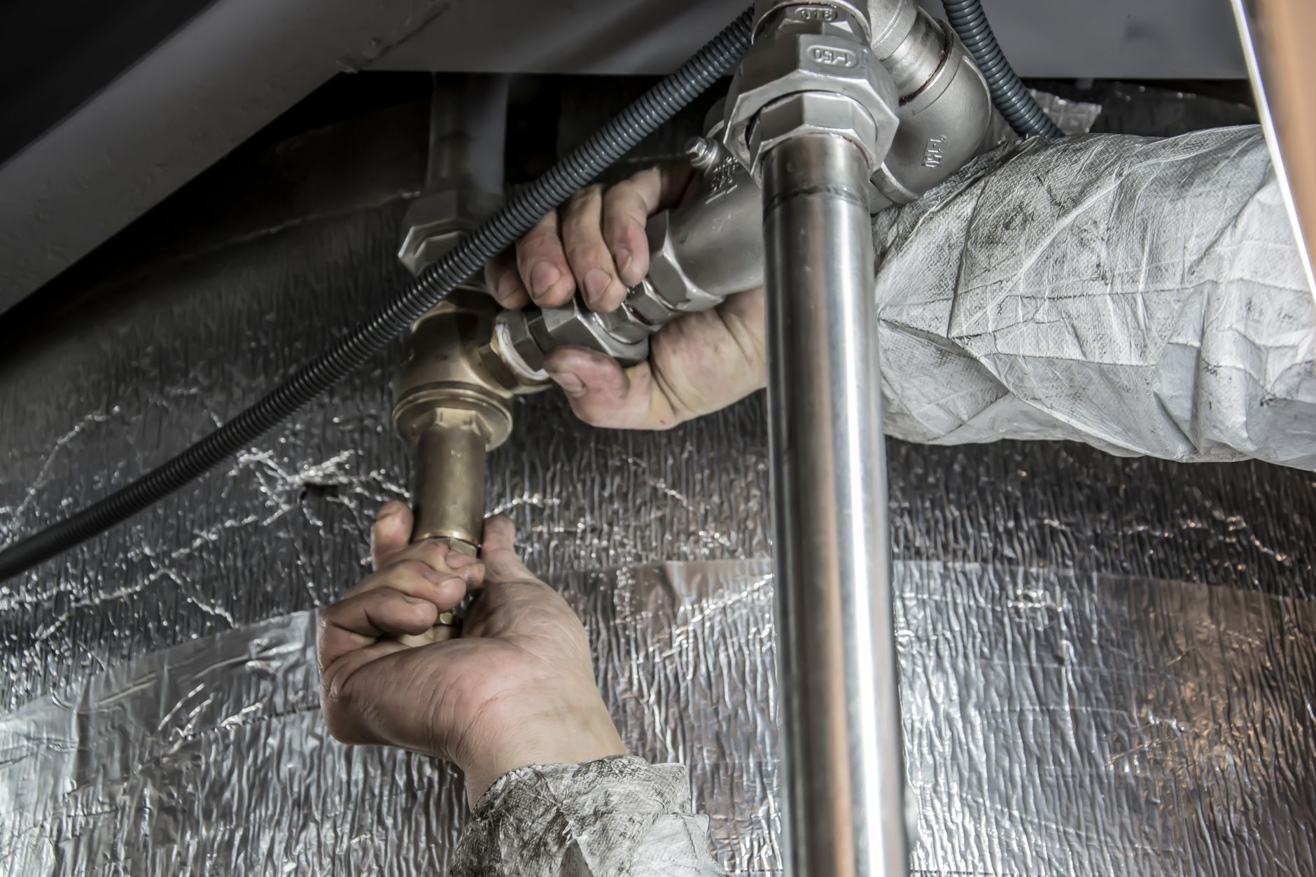 Close-up of hands tightening a brass and steel pipe fitting under insulation